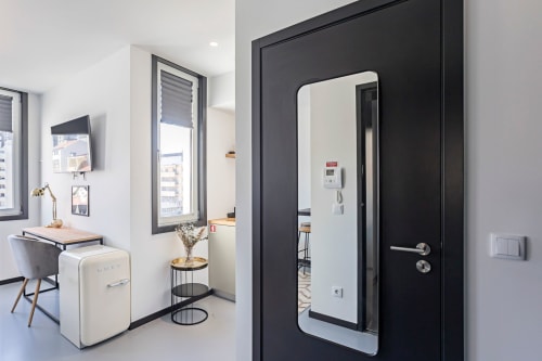 Entrada de estúdio moderno e compacto com porta preta, espelho com moldura branca e mobiliário minimalista em apartamento-hotel no Porto