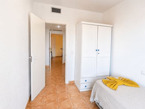 Bedroom in Apartamentos El Calón Playa with white wardrobe, bed with yellow blanket, and terracotta tile flooring