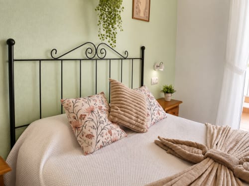 Cómodo dormitorio con cabecero de metal negro decorativo, almohadas florales y ropa de cama beige en Apartamentos El Calón Playa, Cuevas
