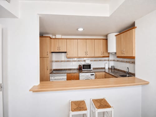 Modern kitchen with wooden cabinets, granite counters, and breakfast bar in Apartamentos El Calón Playa, Cuevas del Almanzora