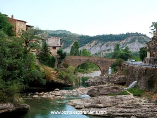 Puente de piedra medieval sobre el río con edificios históricos y las montañas de los Pirineos en Montgat, España