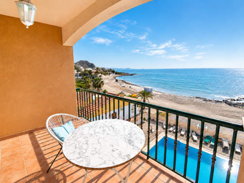 Beachfront apartment balcony with sea view, marble table, white chair, and blue pool at Apartamentos El Calón Playa, Cuevas
