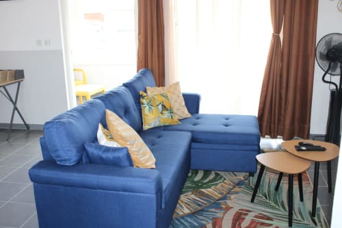 Salon moderne avec canapé sectionnel bleu, coussins jaunes et bleus, tables d'appoint en bois et tapis tropical à T2 Hibiscus