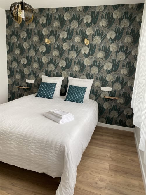 Chambre moderne de l'appartement La Maison Blanche avec papier peint botanique, literie blanche, oreillers bleu-vert et parquet