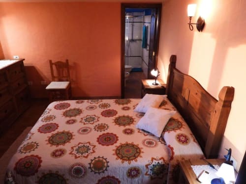 Acogedora habitación de villa en Tijarafe con ropa de cama estampada, muebles de madera, paredes naranja cálidas y baño en suite