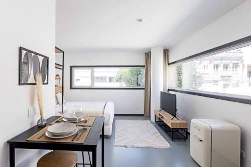 Moderno estúdio no Porto com área de refeições, kitchenette, TV e vistas da cidade pelas grandes janelas