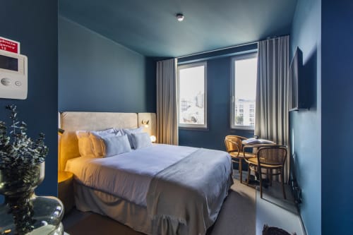 Estúdio compacto e moderno na Benefit Collection Porto com paredes azuis, cama queen, grandes janelas iluminadas, cadeiras de madeira e vista para a cidade