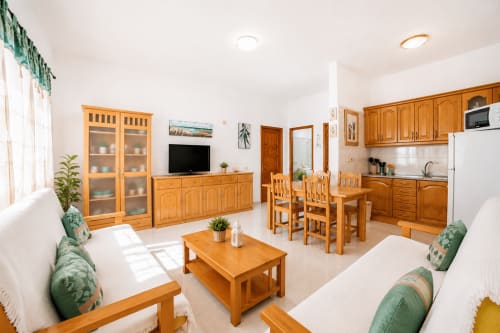 Spacieux séjour lumineux avec mobilier en bois, kitchenette, table à manger et TV dans un appartement près de la plage à Corralejo