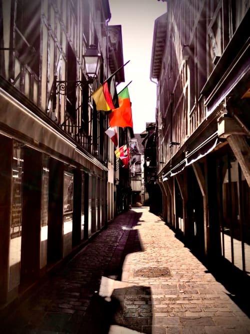 Petite ruelle pavée à Troyes avec bâtiments historiques, lampadaire et drapeaux belge, allemand et français