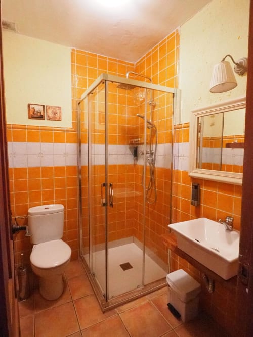 Baño moderno en Rural Senda del Duratón con azulejos naranja y blanco, ducha de cristal, inodoro y lavabo