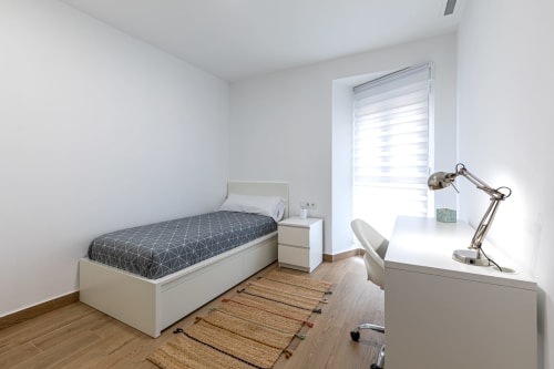 Modern single bedroom at Residencia Demar in Godella with white furnishings, desk, balcony access, and wooden flooring.