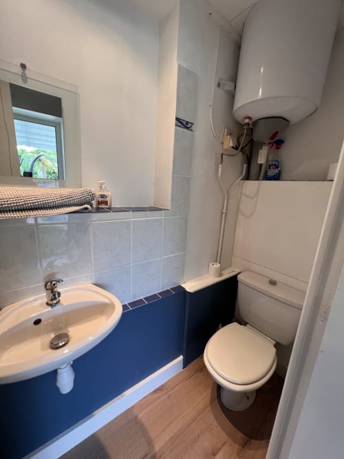Salle de bains du cottage au Restaurant du Port avec lavabo blanc, toilettes et chauffe-eau à Saint Pierre de Boeuf