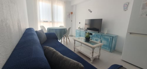 Helles modernes Wohnzimmer mit blauem Sofa, TV, Essbereich und Meerblick in El Médano, Kanarische Inseln