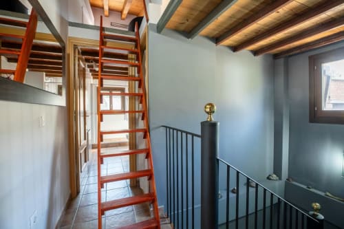 Loft moderno con escalera de madera roja, vigas vistas, barandillas metálicas y vistas a la montaña en Montgat