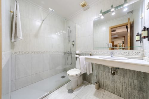 Baño moderno en Hostal El Molino con ducha a ras de suelo, azulejos blancos, tocador de madera y espejo enmarcado