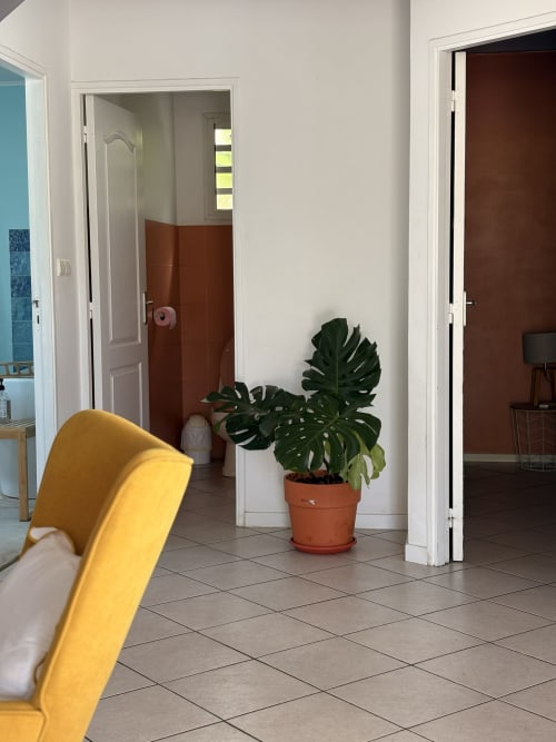 Couloir de villa moderne aux murs blancs, plante en terre cuite, chaise jaune et portes ouvertes à La Villa Maraloupia, Les Avirons