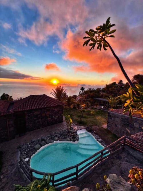 Vista al atardecer de la piscina turquesa de Villa Awara con vistas al océano y palmeras en El Pinillo, La Palma