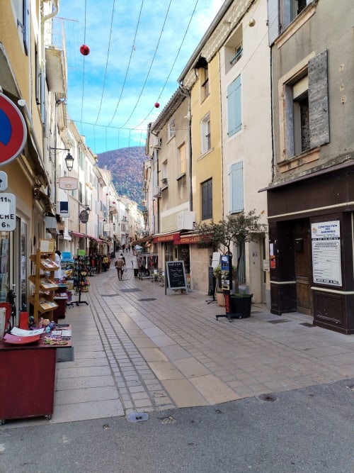 Charming pedestrian street in Venterol, South France near Nyons with colorful buildings, shops, and mountain views.