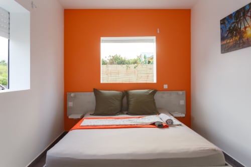 Chambre moderne et lumineuse à la villa Kaz A Bibi à Sainte-Rose avec mur d'accent orange vif, lit queen-size et vue sur le jardin