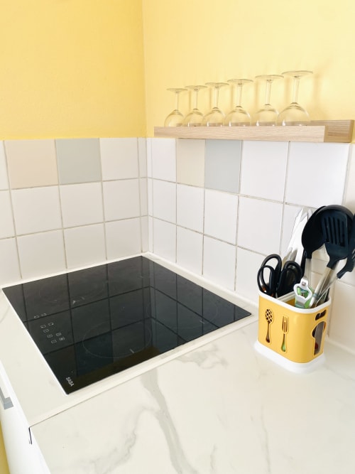 Cuisine moderne avec plaque induction, carrelage blanc métro, mur jaune, support d'ustensiles et verres à vin sur étagère