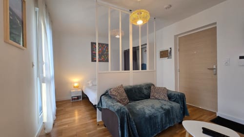 Modern apartment studio at Ô Kastel with sitting area, bed, glass partition, wooden floors and yellow pendant light