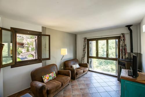 Luminoso salón con sillones de cuero marrón, vistas a la montaña, chimenea y grandes ventanales en apartamento Montgat