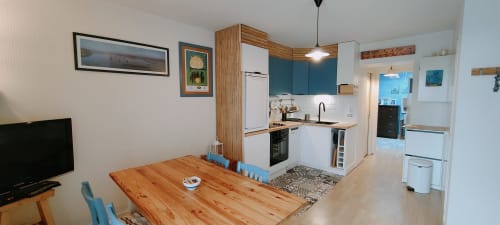 Cuisine ouverte et coin repas de l'appartement Mer et Maisons à La Trinité sur Mer avec table en bois, meubles bleus canard et
