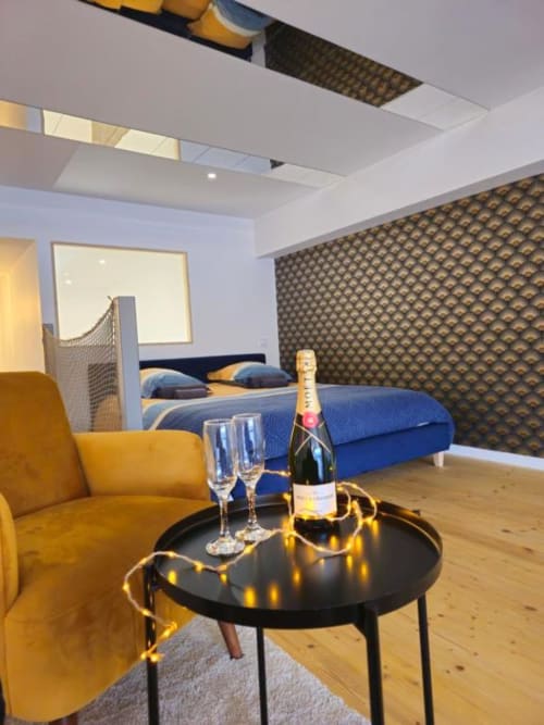 Chambre de luxe avec champagne, fauteuil jaune, lit bleu et mur texturé à Saint-Valery-en-Caux