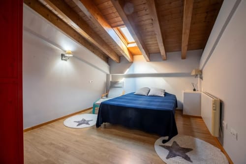 Moderno dormitorio bajo techo con cama azul, vigas de madera, claraboya y vistas a la montaña en Front Beach Apartments, Montgat