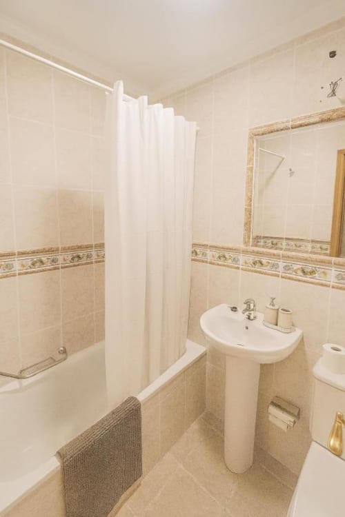 Baño moderno en El HierroStay Apartments con lavamanos pedestal, ducha, bañera y paredes con azulejos beige
