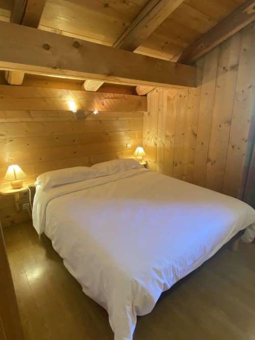 Chambre chaleureuse en bois avec lit queen, draps blancs et ambiance lumineuse à La Ferme des Georgières, Notre-Dame-de-Bellecombe