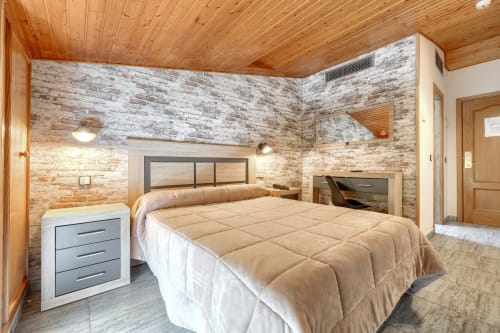 Amplio dormitorio doble en Hostal El Molino, Collado Villalba, con techo de madera, paredes de ladrillo y mobiliario moderno