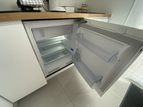 Empty open refrigerator with glass shelves in La Maison Blanche apartment, Bouguenais