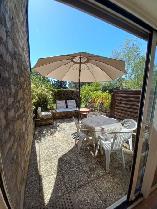 Terrasse ensoleillée de Mer et Maisons avec mobilier blanc, parasol beige et verdure luxuriante à La Trinité sur Mer
