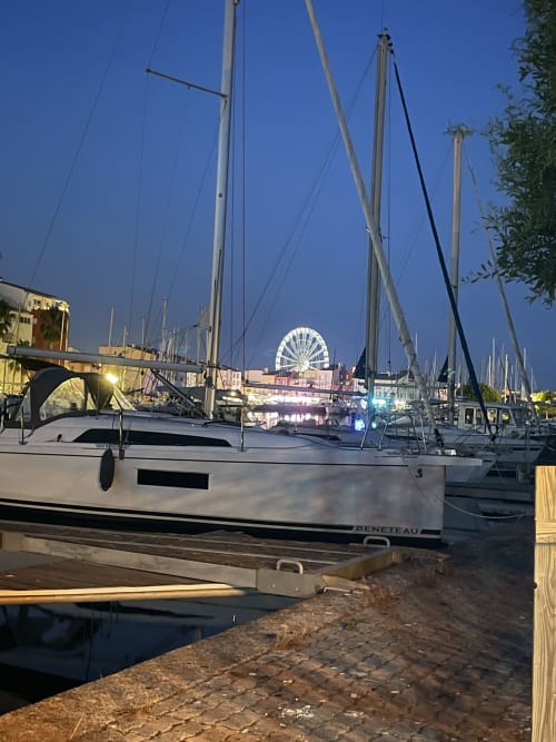 Voilier amarré à la marina de Cap d'Agde au crépuscule avec grande roue illuminée en arrière-plan