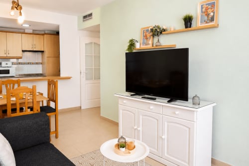 Sala de estar moderna con televisión, mueble blanco para medios, comedor de madera y acceso a cocina en Apartamentos El Calón
