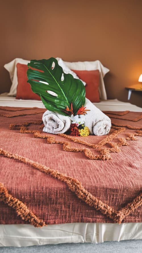 Affichage décoratif de serviettes avec feuille de Monstera tropicale et fleurs sur lit à l'appartement Cocon de Kess, Maisons En Or, Cayenne