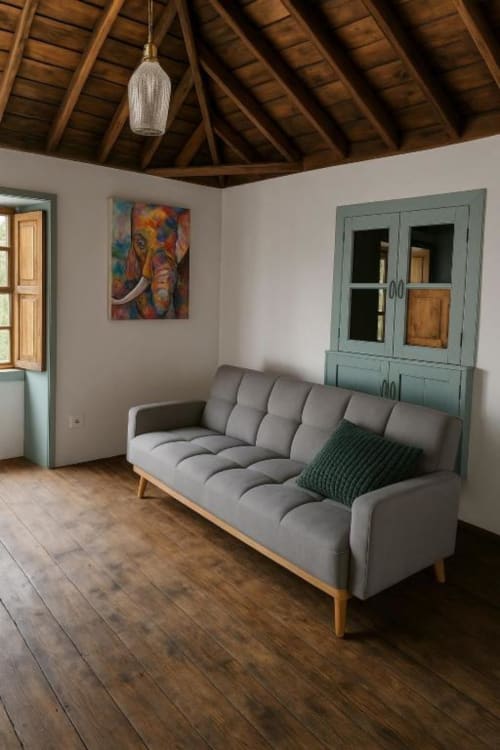 Salón moderno de villa rural en La Palma con sofá gris, vigas de madera, mueble turquesa y obra de arte colorida