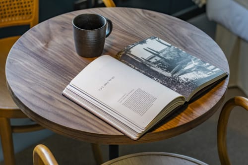 Mesa redonda de madeira em apartamento estúdio no Porto com livro aberto, xícara de café e fotografia.