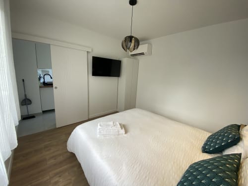 Chambre moderne à La Maison Blanche à Bouguenais avec lit blanc, oreillers vert foncé, TV murale, luminaire suspendu et
