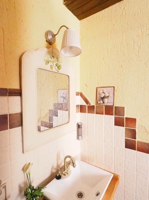 Lavabo con grifo de latón, paredes con azulejos blancos y detalles de terracota, espejo y aplique en Senda del Duratón