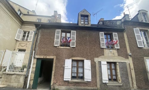 Façade de l'immeuble Le 58 Bayeux avec drapeaux français, volets blancs et façade en brique à Bayeux, France