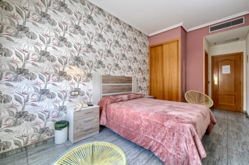 Espaciosa habitación doble en Hostal El Molino con papel tapiz floral, ropa de cama rosa, puertas de madera y mobiliario moderno