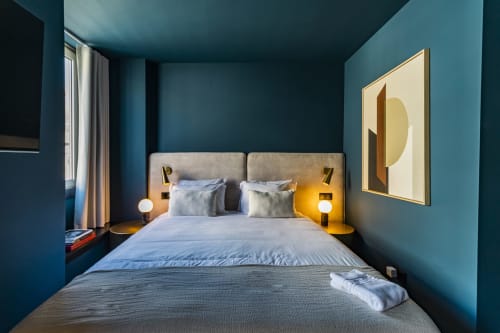 Quarto studio compacto e moderno em hotel no Porto com paredes azul-petróleo, cama, abajures e obra de arte abstrata