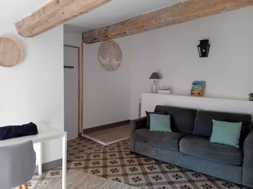 Salon chaleureux du gîte Chez Laure & Marc avec canapé foncé, poutres apparentes, cheminée décorée et carrelage à motifs