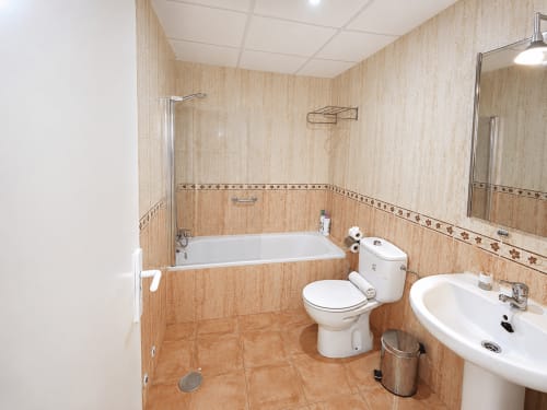 Modern bathroom in Apartamentos El Calón Playa with beige tile walls, bathtub, toilet, sink, and mirror