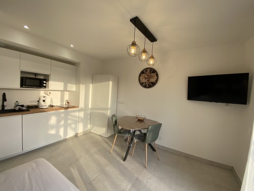Studio moderne à La Maison Blanche avec cuisine blanche, salle à manger, TV murale et luminaires suspendus