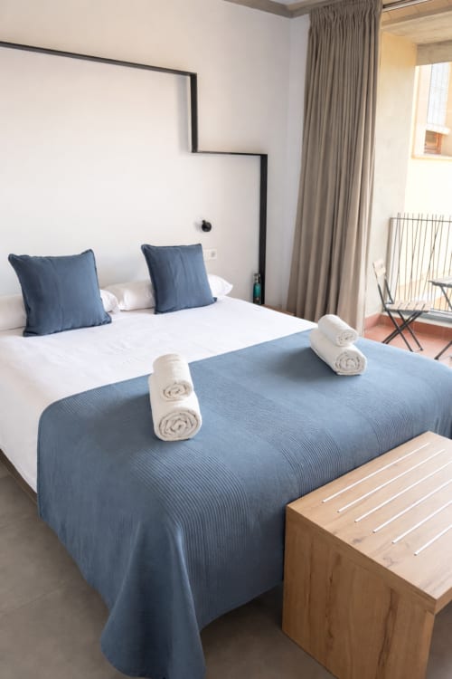 Habitació moderna de l'hotel boutique L'Algars a Tarragona amb accents blaus, vistes a les muntanyes i tovalloles enrotllades al llit