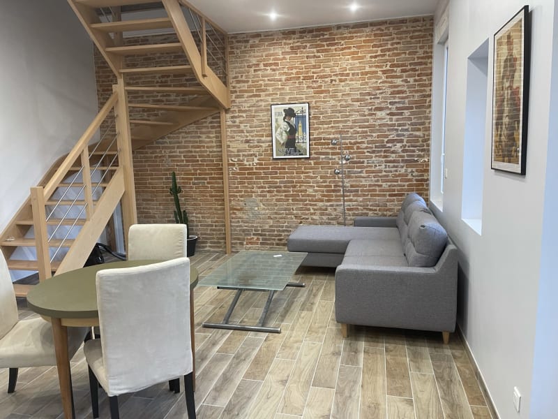 Séjour moderne à la villa Les Gites De Flaubert avec murs en brique apparente, canapé gris, escalier en bois et coin repas