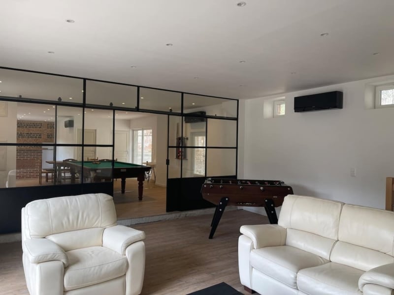 Le salon de la villa Bovary avec sièges en cuir crème, baby-foot et paroi vitrée donnant sur la salle de billard